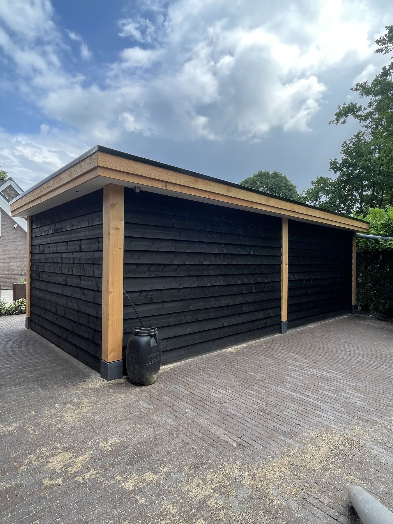 Een schuur met zwarte houten gevelbekleding, eiken boeiboord en staanders