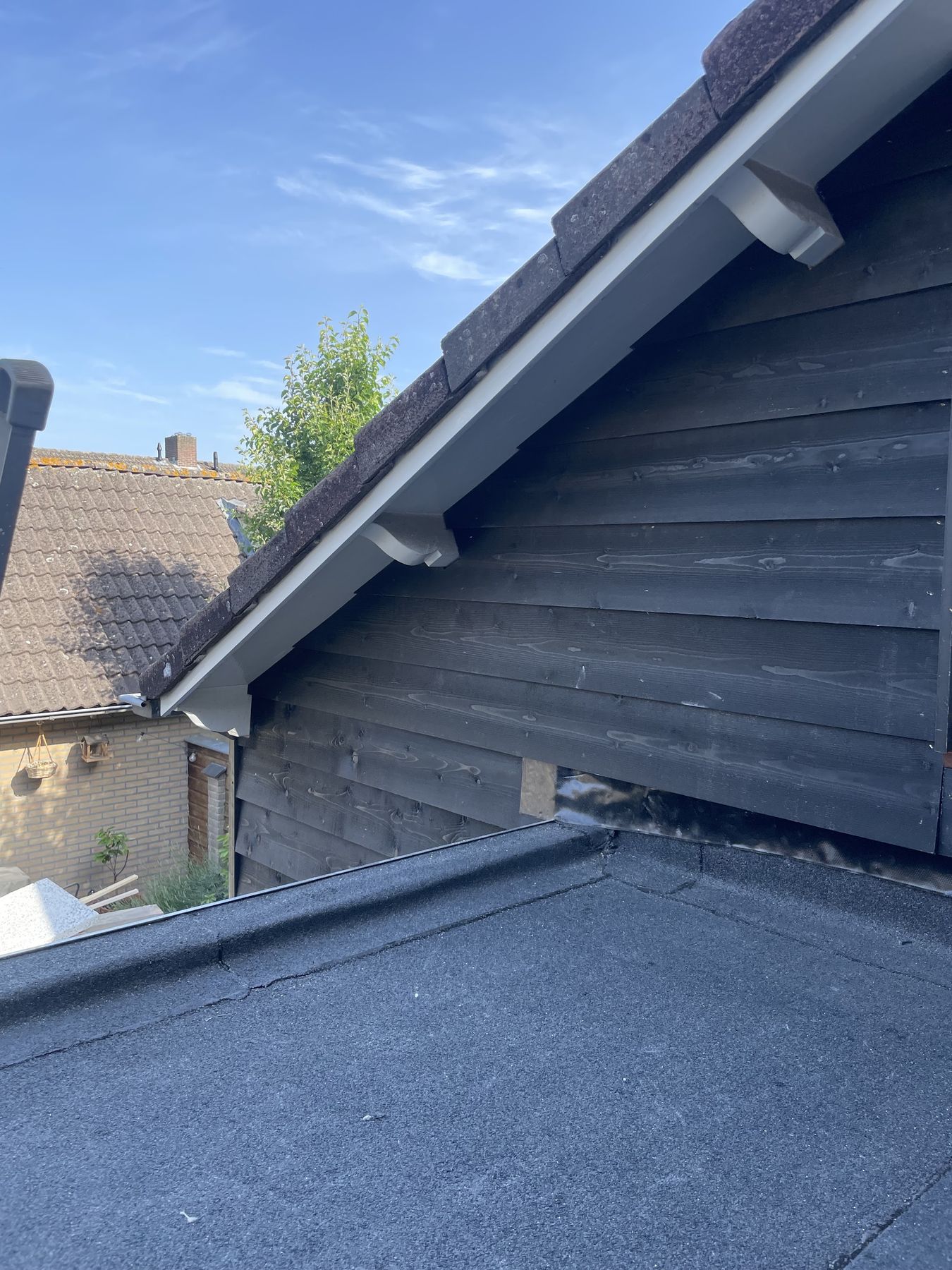 Zwarte houten gevel met een nieuw plat dak ervoor